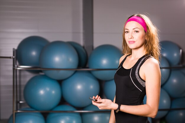 Mujer joven con rastreador de fitness y teléfono inteligente en el gimnasio