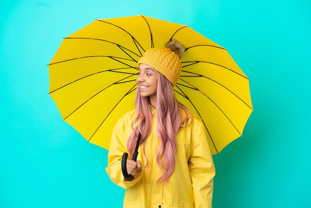 Foto mujer joven de raza mixta con abrigo impermeable y paraguas mirando hacia el lado