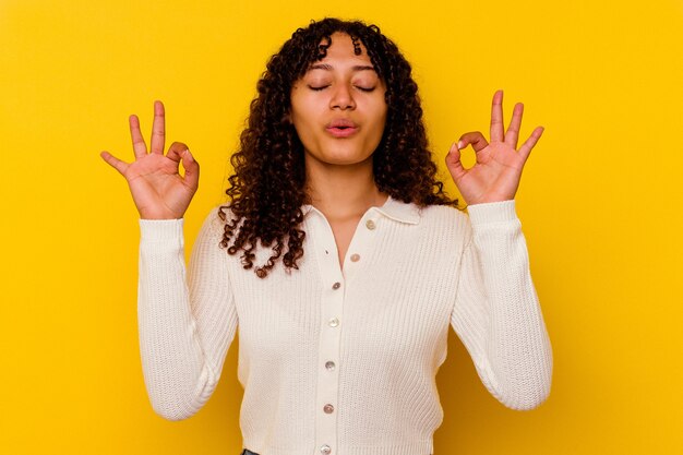 Foto mujer joven de raza mixta aislada en amarillo se relaja después de un duro día de trabajo, ella está realizando yoga.