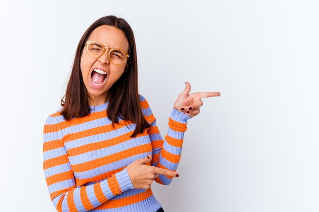 Mujer joven de raza mixta aislada apuntando con los dedos índices a un espacio de copia, expresando entusiasmo y deseo.