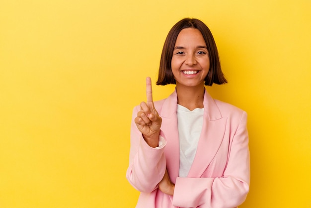 Mujer joven de raza mixta aislada de fondo amarillo que muestra el número uno con el dedo.