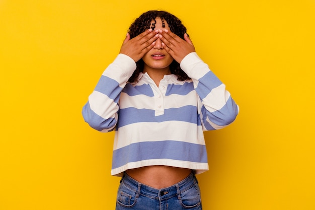 Mujer joven de raza mixta aislada en la pared amarilla miedo cubrirse los ojos con las manos.