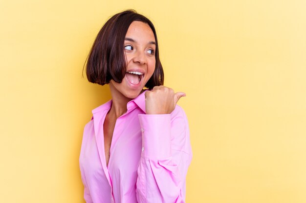 Mujer joven de raza mixta aislada en puntos de fondo amarillo con el dedo pulgar lejos, riendo y despreocupado.