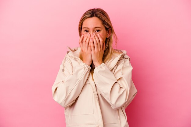 Mujer joven de raza mixta aislada en rosa riendo de algo, cubriendo la boca con las manos.