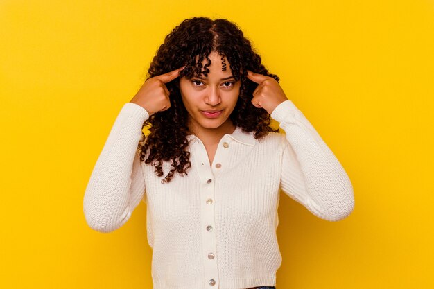 Mujer joven de raza mixta aislada sobre fondo amarillo se centró en una tarea, manteniendo los dedos índice apuntando la cabeza.