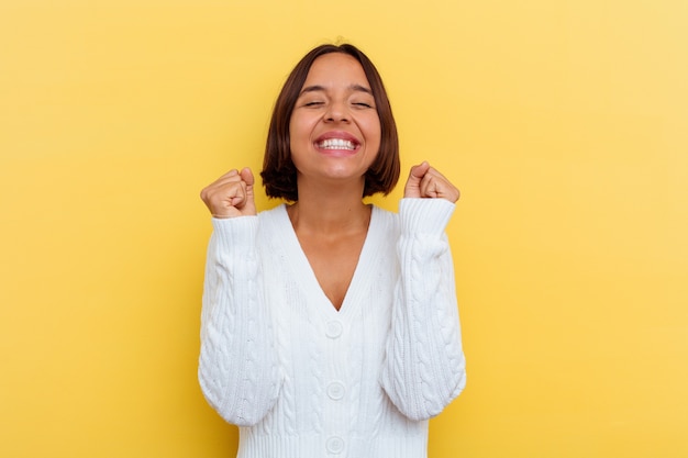 Mujer joven de raza mixta aislada sobre fondo amarillo levantando el puño, sintiéndose feliz y exitoso. Concepto de victoria.