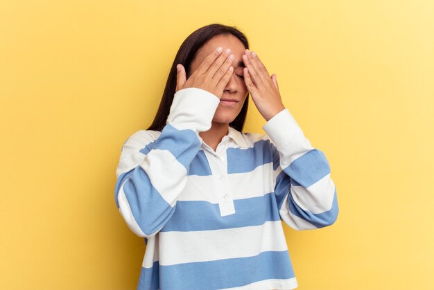 Mujer joven de raza mixta aislada sobre fondo amarillo miedo cubrirse los ojos con las manos.