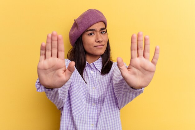 Mujer joven de raza mixta aislada sobre fondo amarillo de pie con la mano extendida mostrando la señal de stop, impidiéndote.