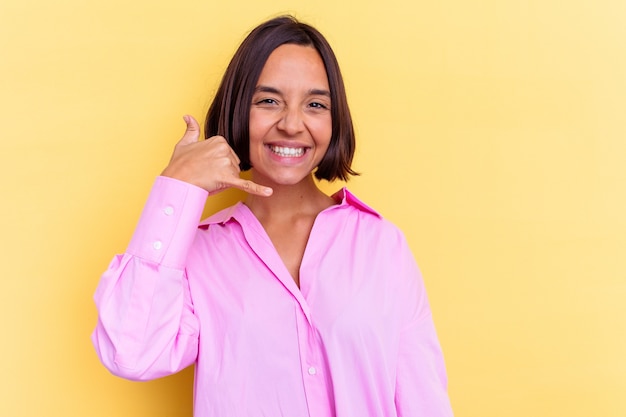 Mujer joven de raza mixta aislada sobre fondo amarillo que muestra un gesto de llamada de teléfono móvil con los dedos.