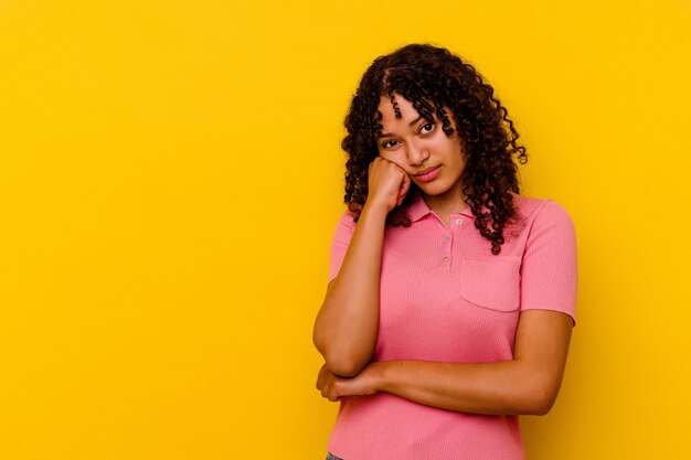 Mujer joven de raza mixta aislada sobre fondo amarillo que se siente triste y pensativa, mirando el espacio de la copia.