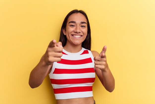 Mujer joven de raza mixta aislada sobre fondo amarillo sonrisas alegres apuntando al frente.