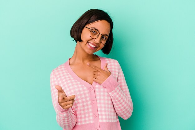 Mujer joven de raza mixta aislada sobre fondo azul sonrisas alegres apuntando al frente.