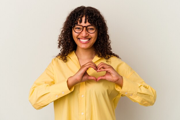 Mujer joven de raza mixta aislada sobre fondo blanco sonriendo y mostrando una forma de corazón con las manos.