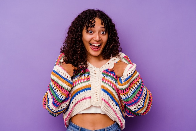 Mujer joven de raza mixta aislada sobre fondo púrpura sorprendido señalando con el dedo, sonriendo ampliamente.