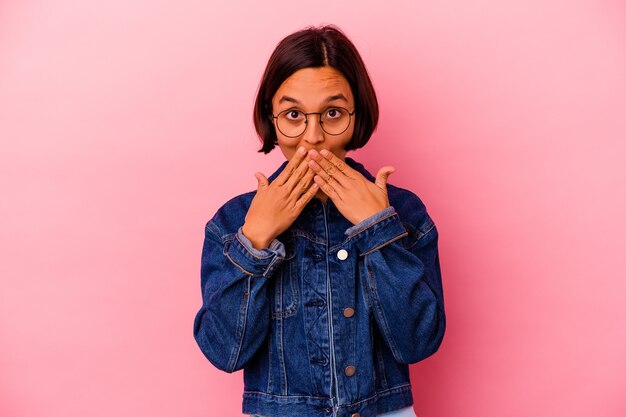 Mujer joven de raza mixta aislada sobre fondo rosa conmocionado cubriendo la boca con las manos.