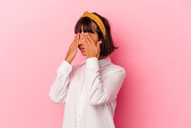 Mujer joven de raza mixta aislada sobre fondo rosa miedo cubrirse los ojos con las manos.