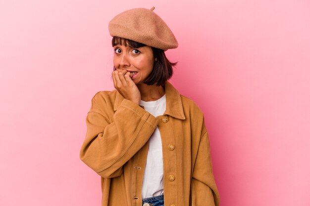 Mujer joven de raza mixta aislada sobre fondo rosa mordiéndose las uñas, nerviosa y muy ansiosa.