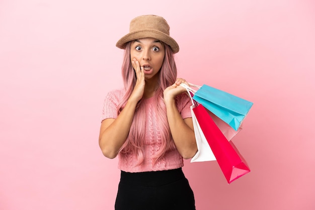Mujer joven de raza mixta con bolsa de compras aislada sobre fondo rosa con sorpresa y expresión facial conmocionada