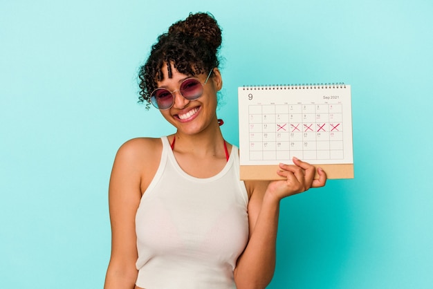 Mujer joven de raza mixta con calendario aislado sobre fondo azul feliz, sonriente y alegre.