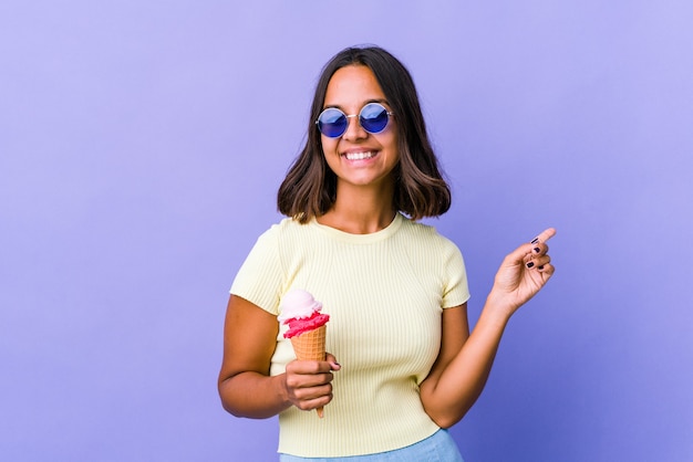 Mujer joven de raza mixta comiendo un helado apuntando a diferentes espacios de copia, eligiendo uno de ellos, mostrando con el dedo.