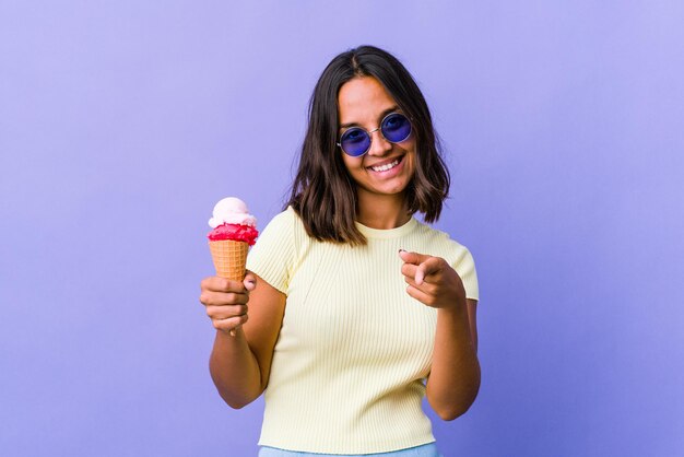 Mujer joven de raza mixta comiendo un helado sonrisas alegres apuntando al frente.