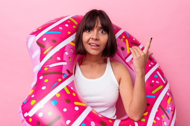 Foto mujer joven de raza mixta con donut inflable aislado sobre fondo rosa mostrando un gesto de decepción con el dedo índice.