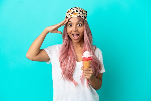 Mujer joven de raza mixta con un helado de cucurucho aislado sobre fondo azul con expresión de sorpresa