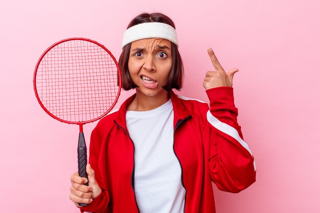 Mujer joven de raza mixta jugando al bádminton aislado en la pared rosada mostrando un gesto de decepción con el dedo índice.