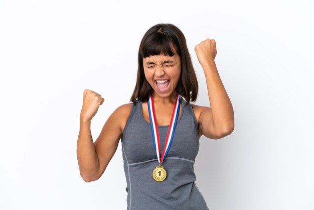 Mujer joven de raza mixta con medallas aislado sobre fondo blanco celebrando una victoria