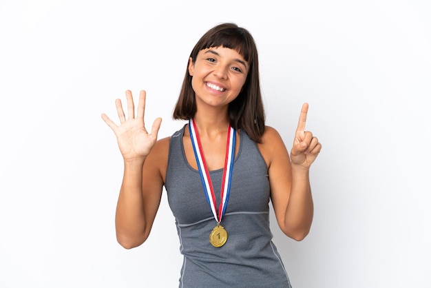 Mujer joven de raza mixta con medallas aislado sobre fondo blanco contando seis con los dedos