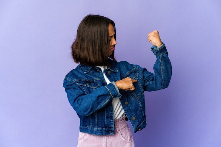 Foto mujer joven de raza mixta mostrando gesto de fuerza con los brazos, símbolo del poder