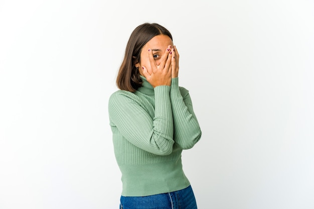 Foto mujer joven de raza mixta parpadear entre los dedos asustada y nerviosa.