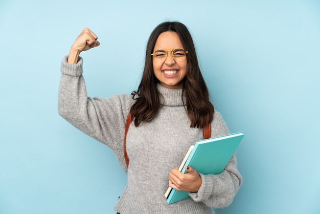 Mujer joven de raza mixta que va a la escuela en la pared azul haciendo un gesto fuerte