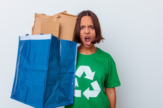 Mujer joven de raza mixta reciclando cartón aislado en la pared blanca gritando muy enojado y agresivo.