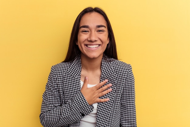 Mujer joven de raza mixta se ríe a carcajadas manteniendo la mano en el pecho.