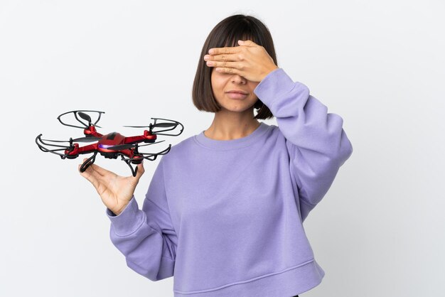 Mujer joven de raza mixta sosteniendo un avión no tripulado aislado sobre fondo blanco cubriendo los ojos con las manos. No quiero ver algo