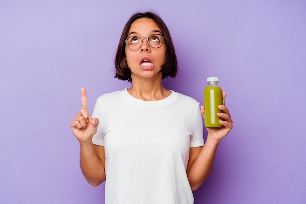 Mujer joven de raza mixta sosteniendo un batido saludable aislado sobre fondo púrpura apuntando al revés con la boca abierta.