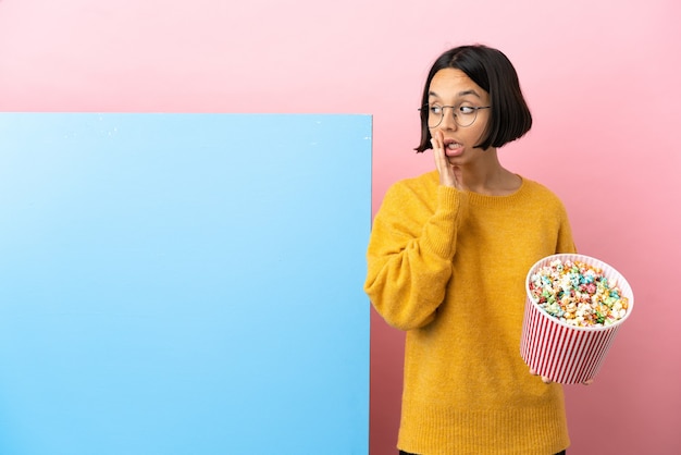 Mujer joven de raza mixta sosteniendo palomitas de maíz con una gran pancarta aislada