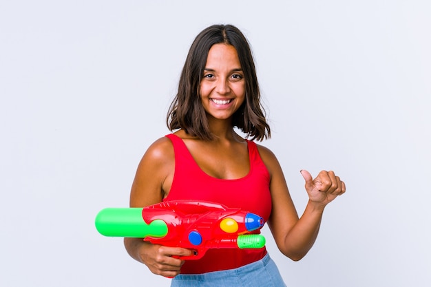 Mujer joven de raza mixta sosteniendo una pistola de agua aislada levantando ambos pulgares, sonriente y confiada.