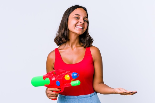 Mujer joven de raza mixta sosteniendo una pistola de agua aislada mostrando una expresión de bienvenida.