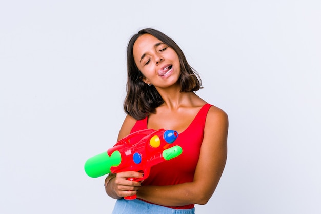 Mujer joven de raza mixta sosteniendo una pistola de agua aislado divertido y amistoso sacando la lengua.