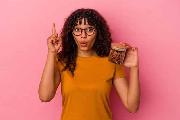 Mujer joven de raza mixta sosteniendo un tarro de almendras aislado en la pared rosa con una gran idea, concepto de creatividad.