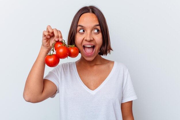 Mujer joven de raza mixta sosteniendo tomates aislados en la pared blanca