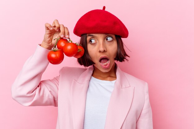 Mujer joven de raza mixta sosteniendo tomates aislados en la pared rosa