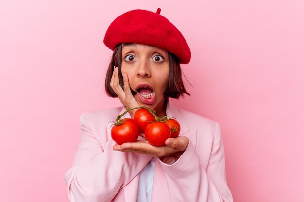 Mujer joven de raza mixta sosteniendo tomates aislados en la pared rosa