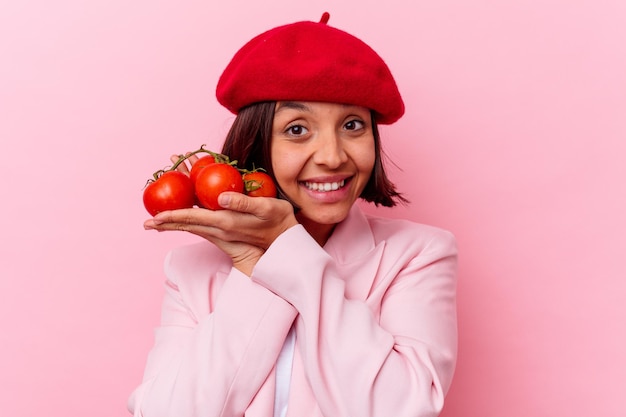 Mujer joven de raza mixta sosteniendo tomates aislados en la pared rosa