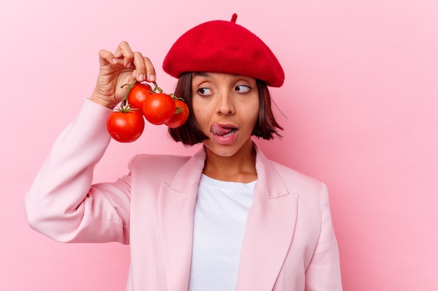 Mujer joven de raza mixta sosteniendo tomates aislados en la pared rosa