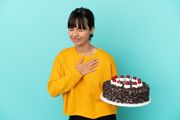 Mujer joven de raza mixta sosteniendo la torta de cumpleaños con un dolor en el corazón