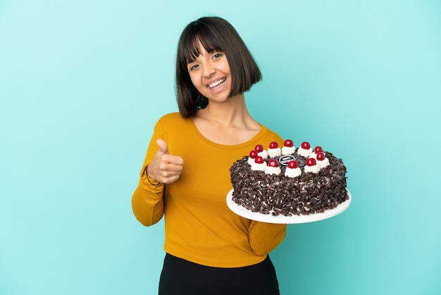 Mujer joven de raza mixta sosteniendo la torta de cumpleaños con los pulgares hacia arriba porque ha sucedido algo bueno