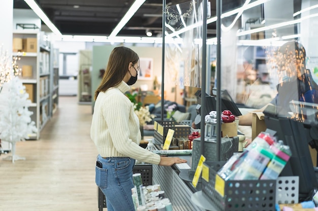 Mujer joven realiza el check out usando el teléfono a través del terminal en la tienda distanciamiento social